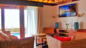 Una habitación con muebles de mimbre, vista a la piscina y un televisor que muestra una playa.