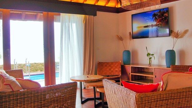 Una habitación con muebles de mimbre, vista a la piscina y un televisor que muestra una playa.