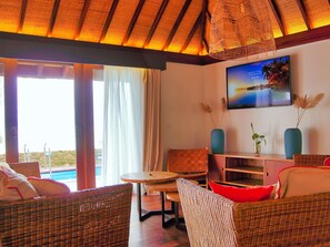 A room with wicker furniture, a pool view, and a TV displaying a beach scene.