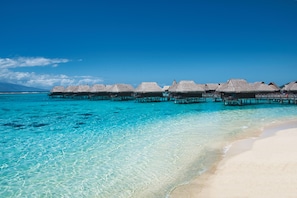 Cabañas sobre el agua con techos de paja, agua turquesa cristalina y una playa de arena.