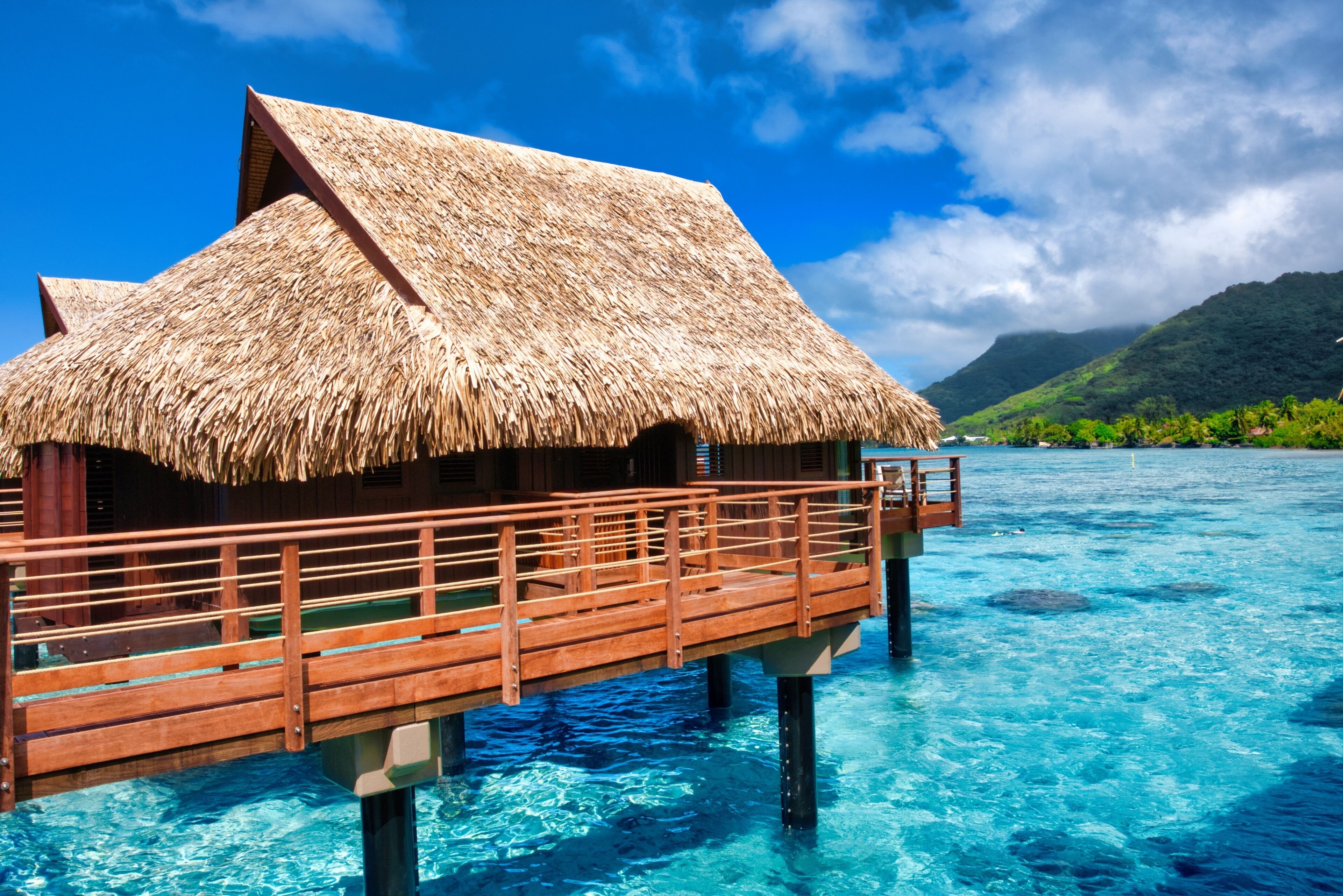 A thatched-roof overwater bungalow with a wooden deck extending into clear blue water.
