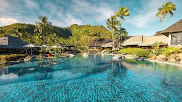A resort with a clear pool, palm trees, and thatched-roof buildings.