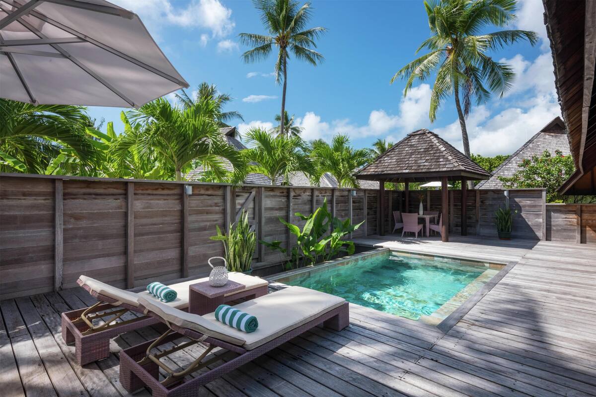 A wooden deck with a pool, lounge chairs, and a gazebo.