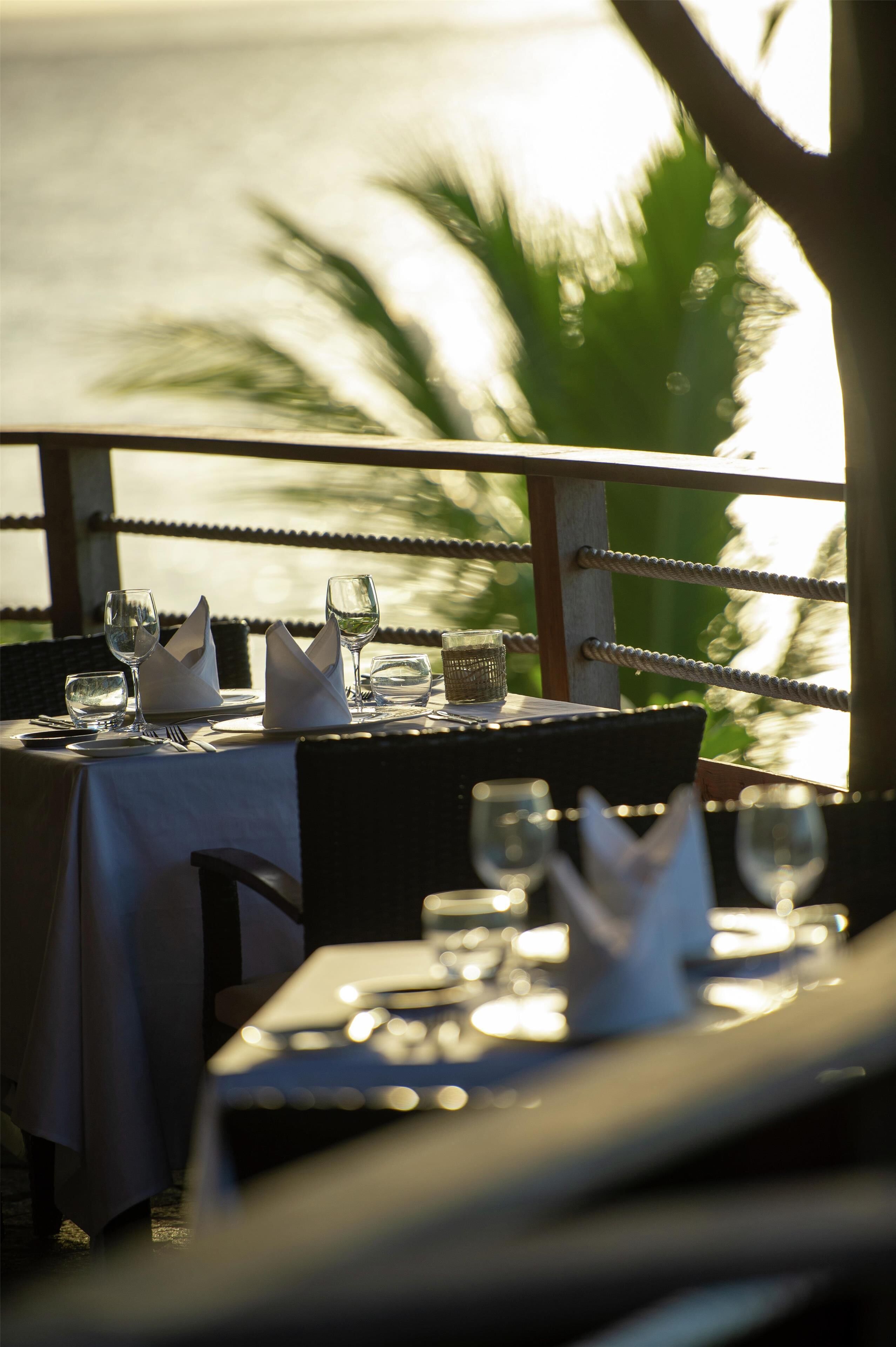 Une table dressée pour le dîner, avec vue sur la mer et les palmiers.