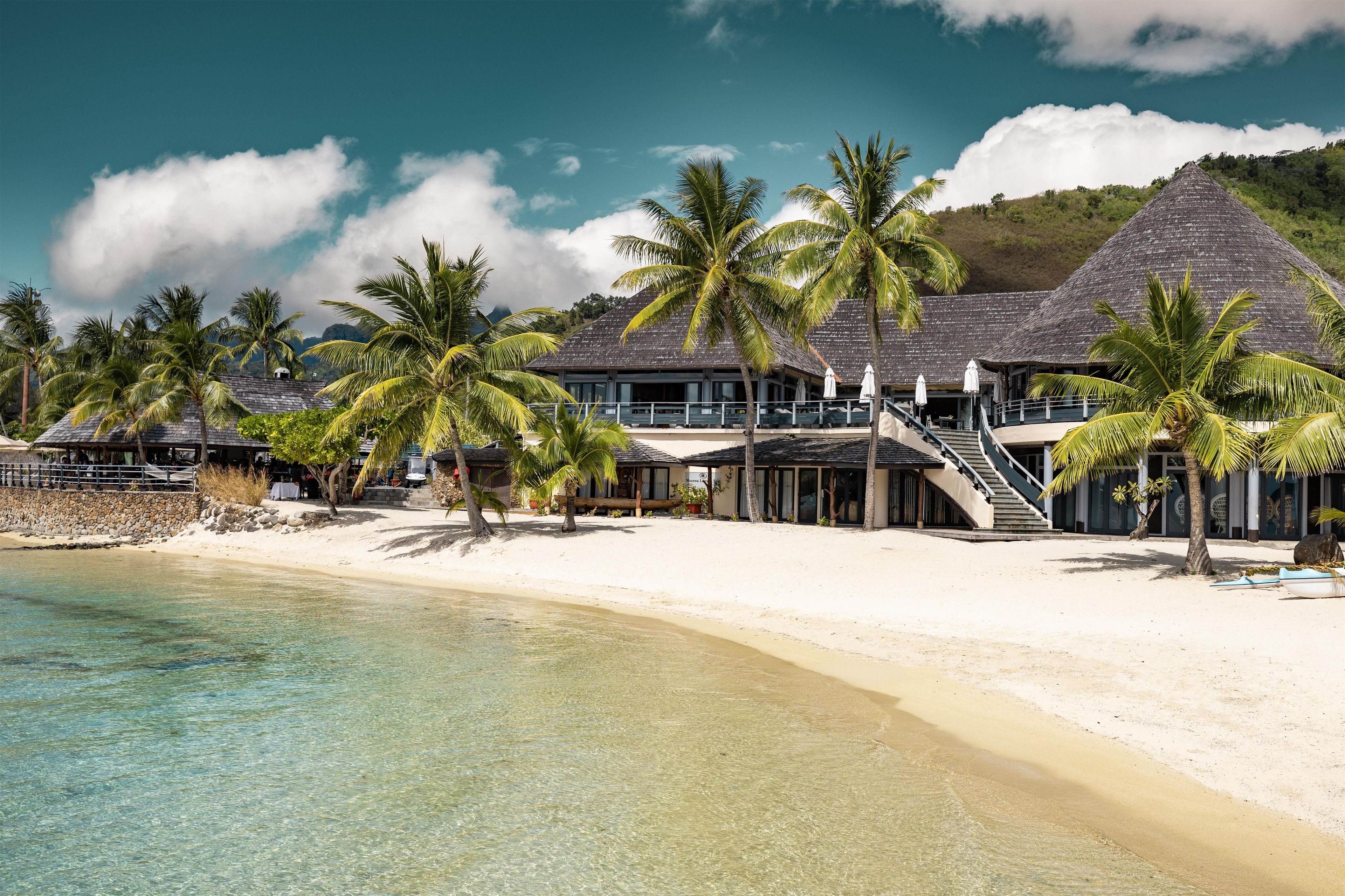 A beachfront resort with multiple overwater bungalows, palm trees, and clear turquoise waters.