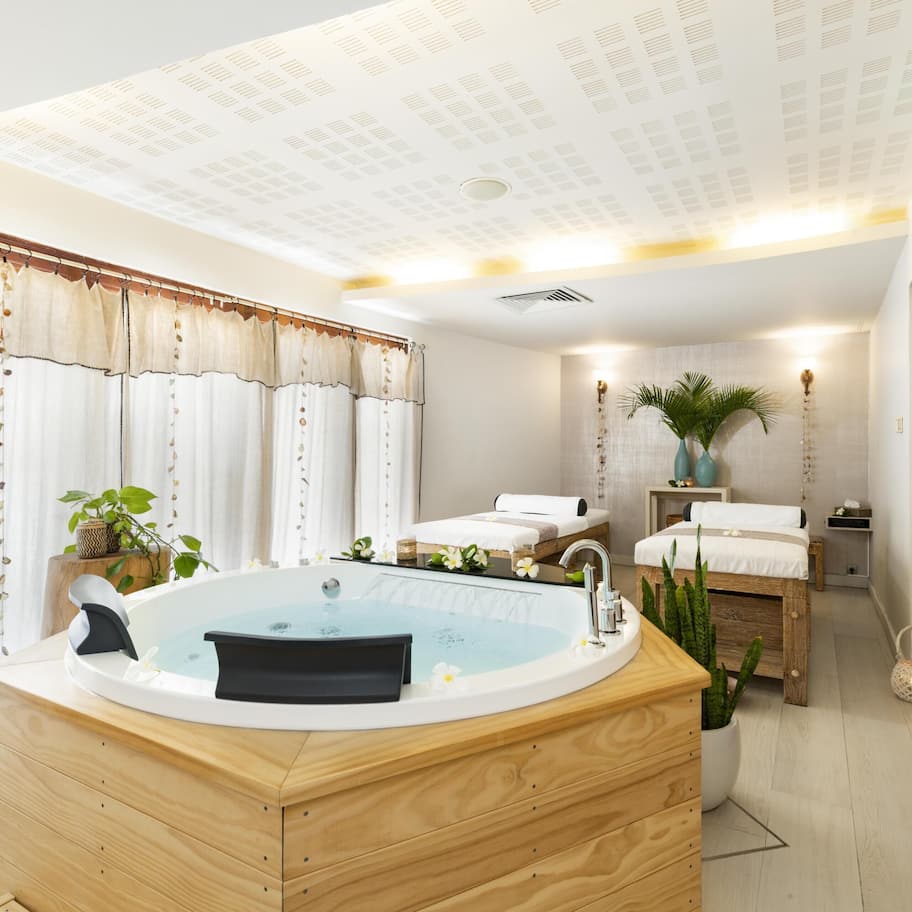 A modern bathroom with a freestanding bathtub, a wooden vanity, a small seating area, and a shower area.