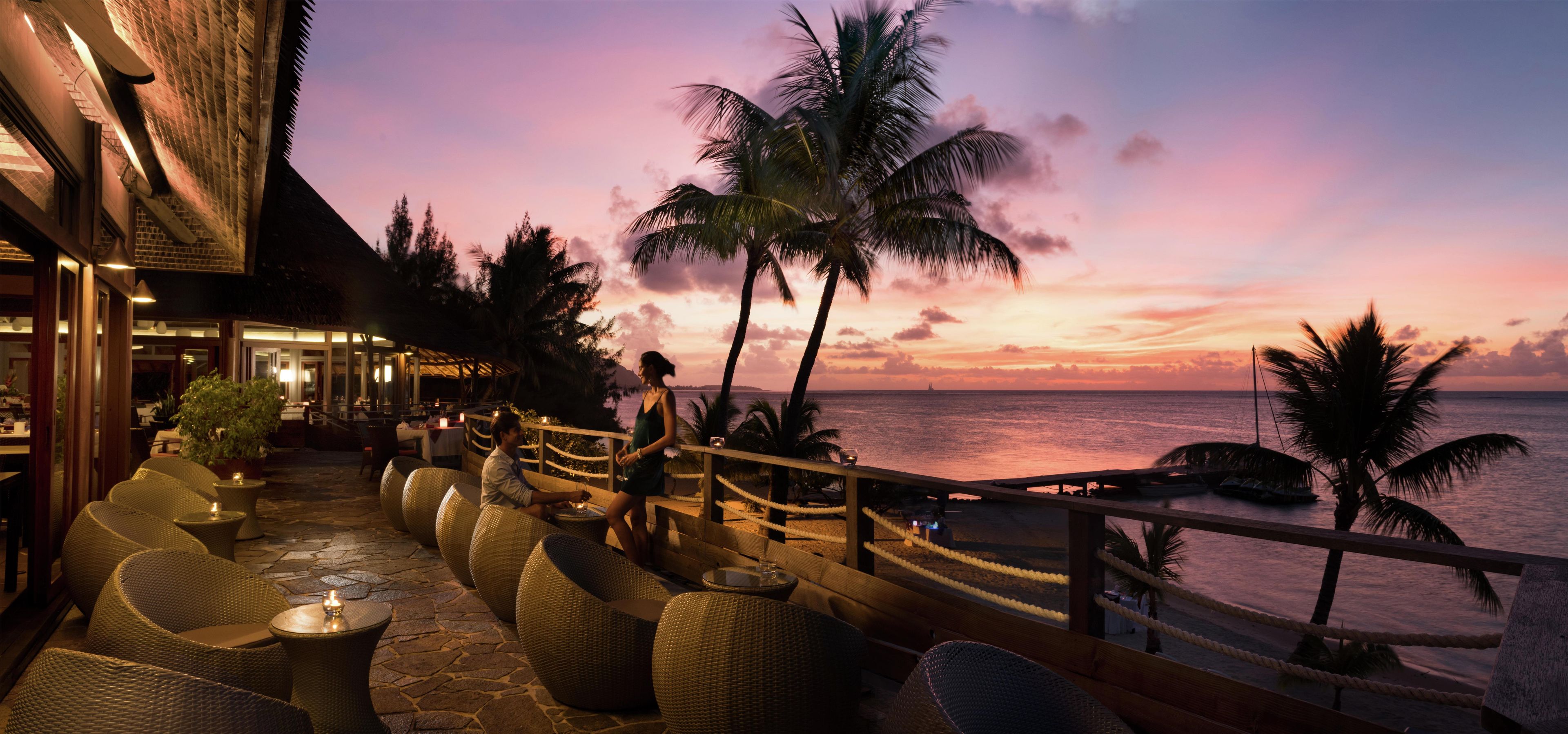 Un restaurant en bord de mer avec une terrasse, des palmiers et une vue sur l’océan.