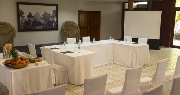 A conference room with a long table, white chairs, and a fruit bowl.
