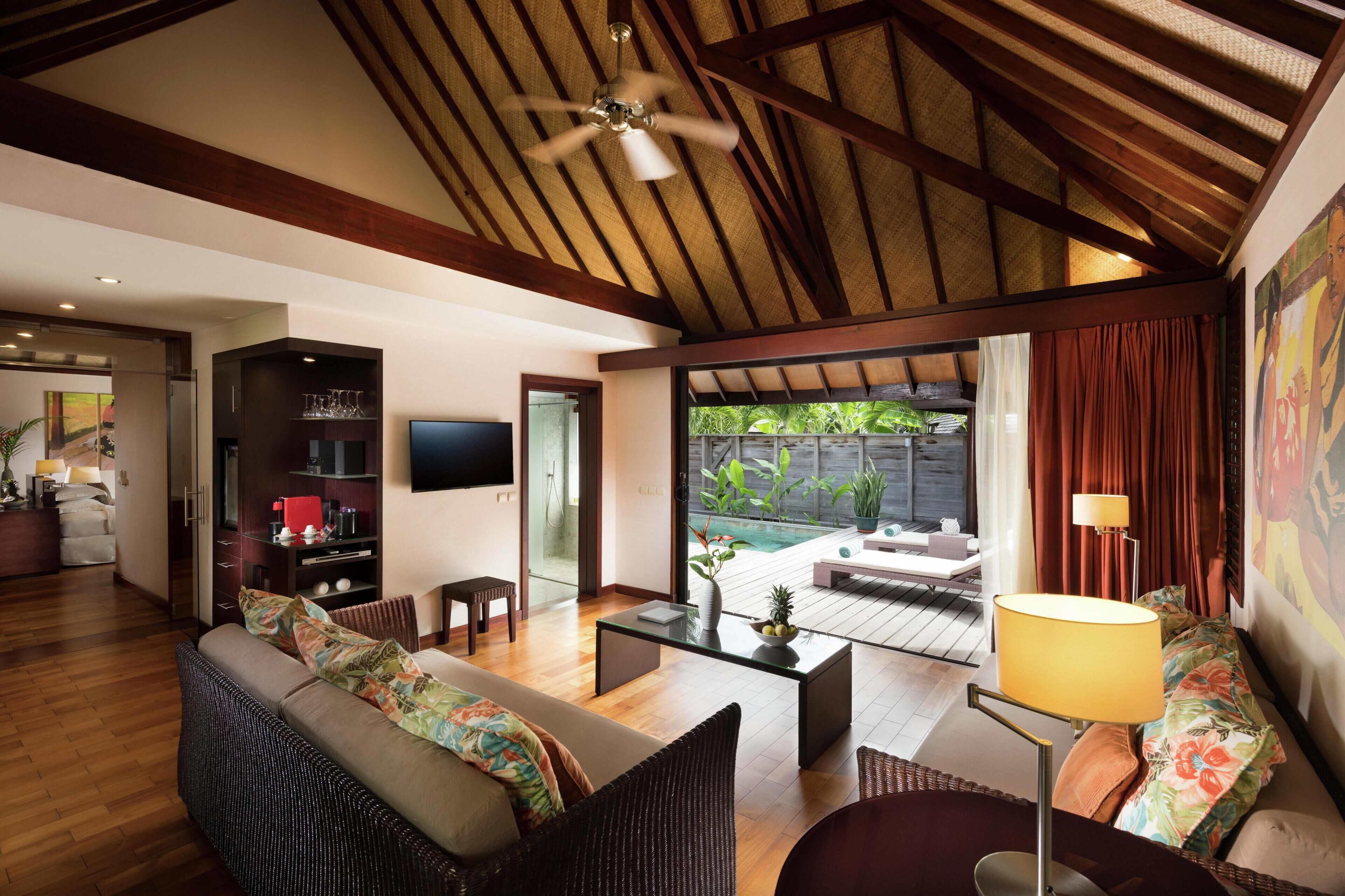 A modern living room with a ceiling fan, wooden beams, a sofa, a coffee table, and a TV.
