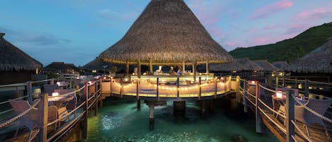 An overwater bungalows with thatched roofs, clear water, and wooden walkways.