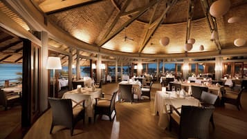 Een restaurant met ronde tafels, rieten stoelen en uitzicht op zee.