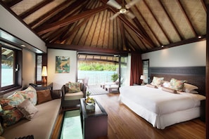 A bedroom with a large bed, a sofa, a coffee table, and a view of a pool.