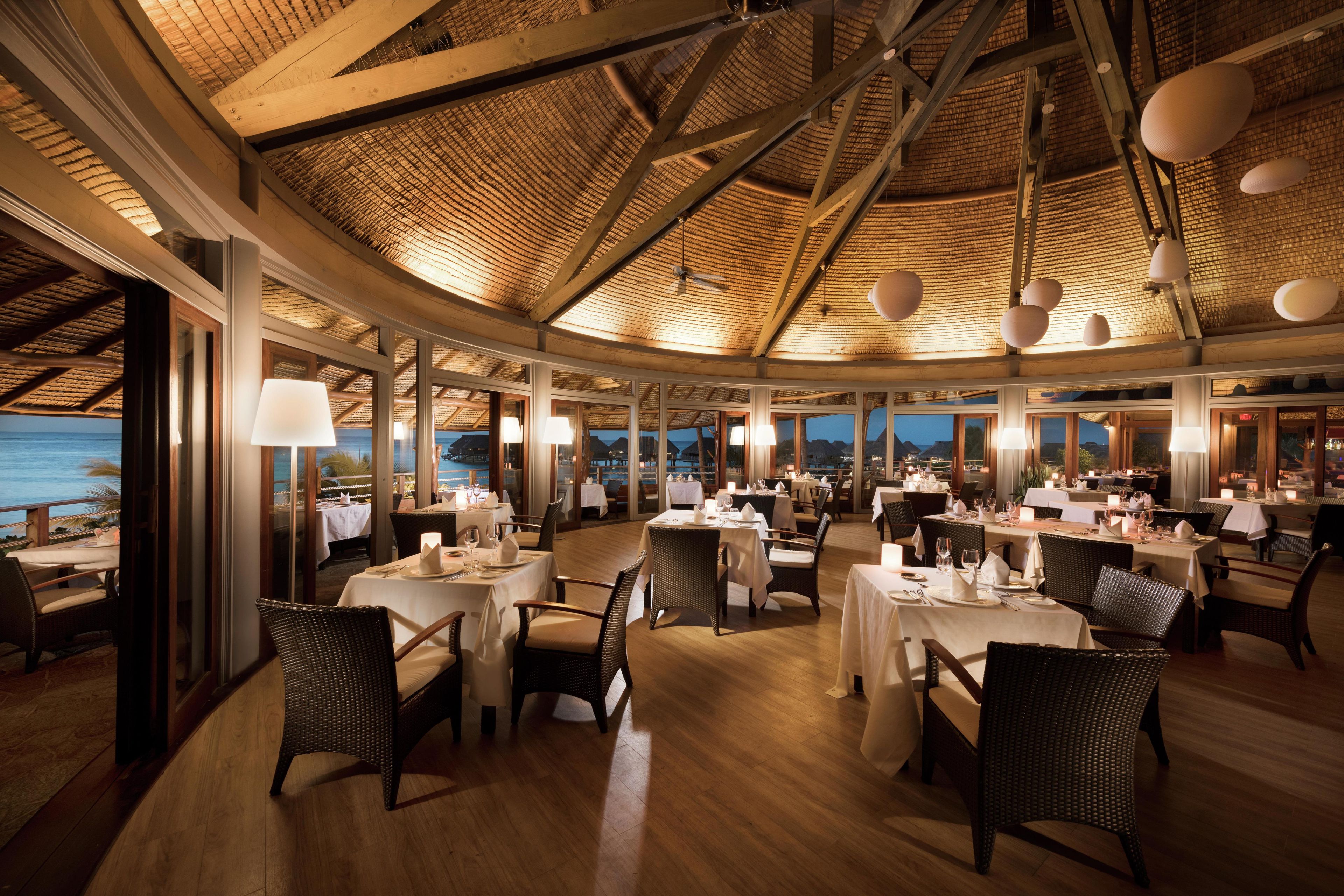 A restaurant with round tables, wicker chairs, and a view of the sea.