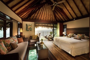 A room with a bed, a sofa, a coffee table, a ceiling fan, and a view of the sea.