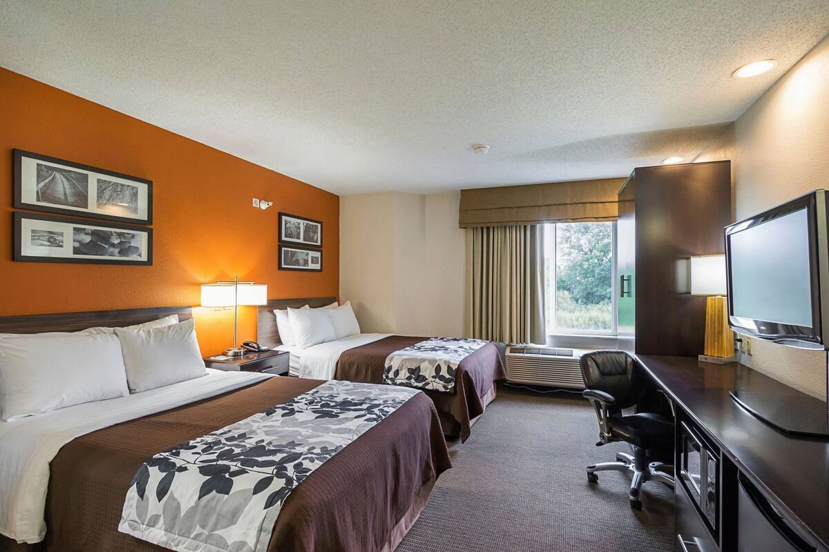 A hotel room with two beds, a desk, a chair, a television, and framed pictures on the wall.