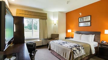 A hotel room with a bed, desk, chair, TV, and a window with curtains.