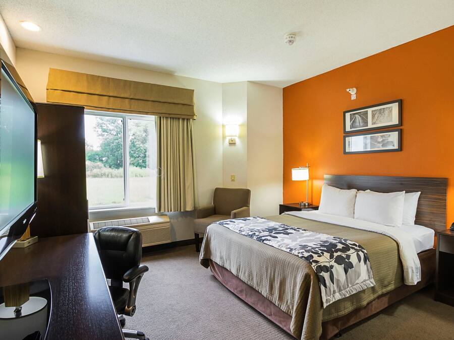 A hotel room with a bed, desk, chair, TV, and a window with curtains.