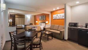 A hotel room with a bed, a sofa, a dining table with chairs, a kitchen area with a microwave and coffee maker, and artwork on the walls. - Sleep Inn And Suites Danville (Danville)