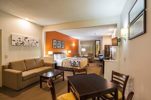 A hotel room with a sofa, a bed, a table, and chairs. There are wall-mounted lamps and framed pictures. - Sleep Inn And Suites Danville (Danville)