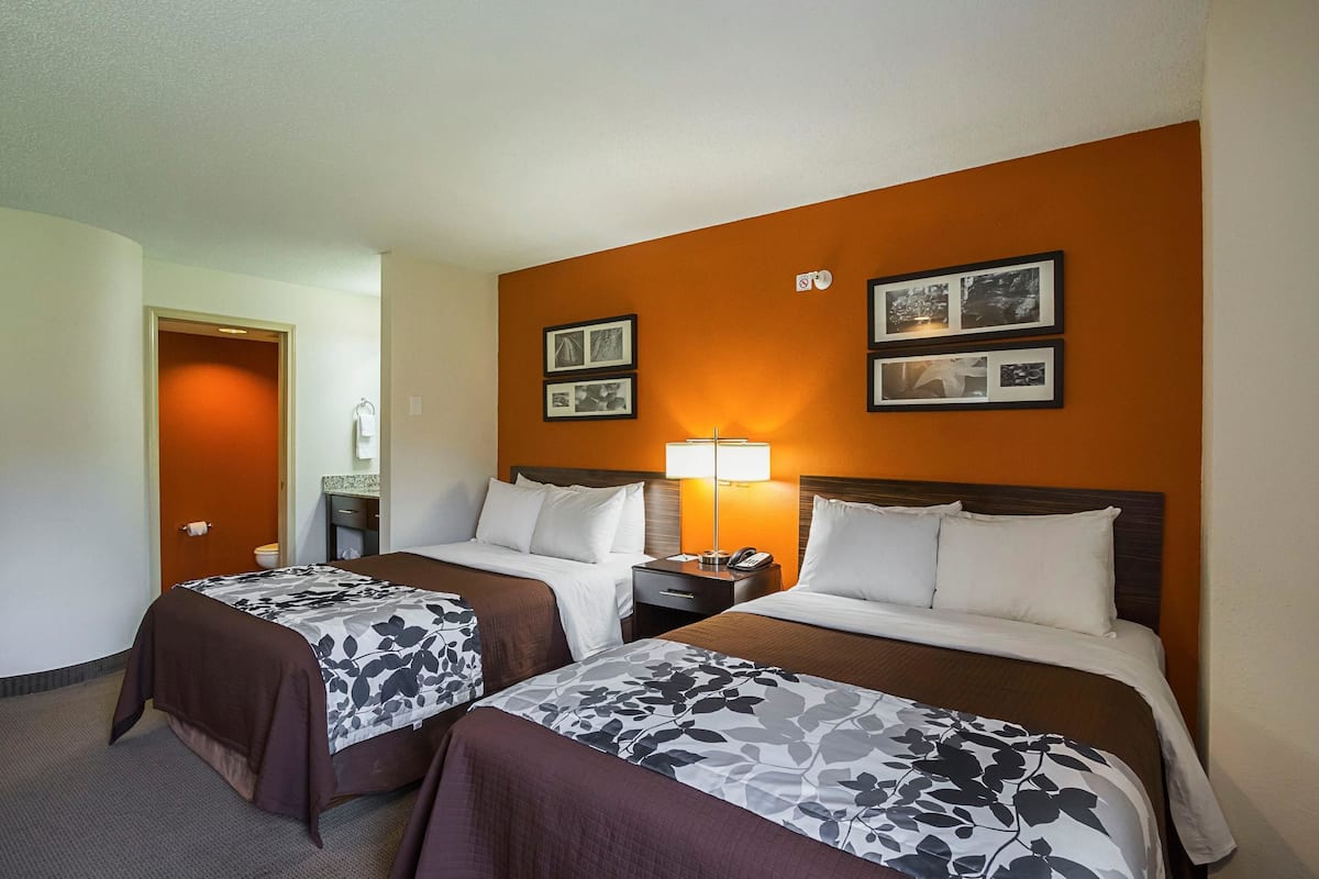 A hotel room with two beds, a nightstand, a lamp, and framed pictures on the wall.