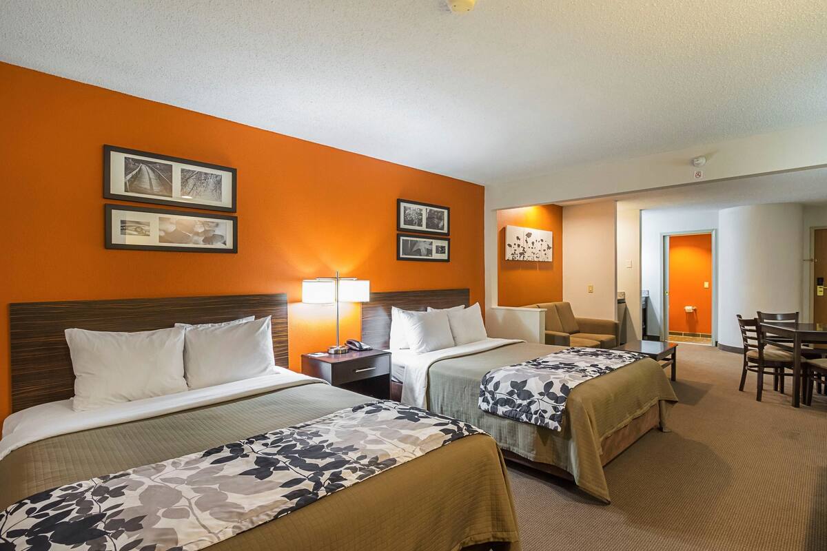 A hotel room with two beds, a desk, and a dining area.
