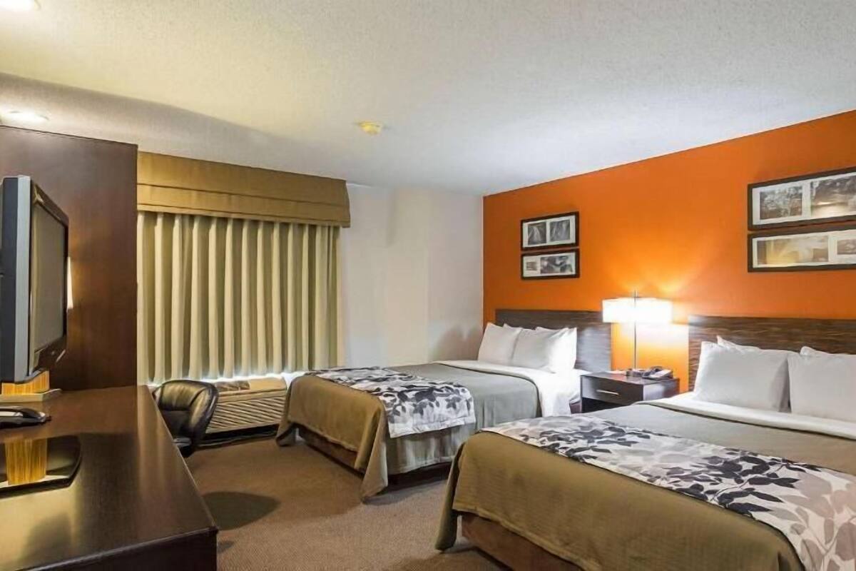 A hotel room with two beds, a desk, a television, and a window with blinds.