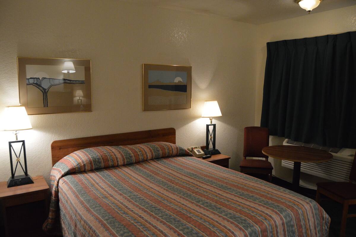 A hotel room with a large bed, two bedside lamps, a chair, a small table, and two framed pictures on the wall.