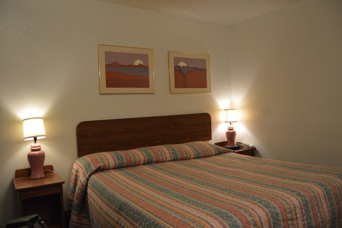 A hotel room with a wooden headboard, a striped bedspread, two bedside lamps, and two framed pictures on the wall.