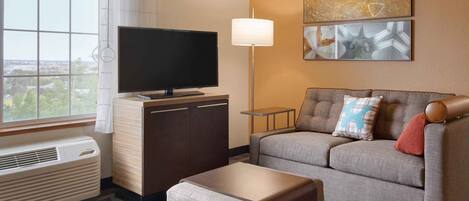 Hotelkamer met een flatscreen televisie, een bank, een klein bijzettafeltje, een lamp en een groot raam met uitzicht.