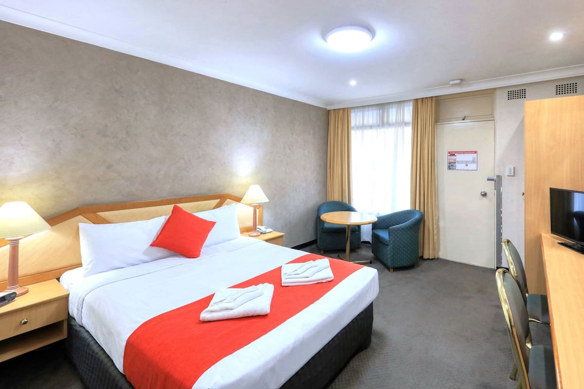 Een hotelkamer met een bed, nachtkastjes, een bureau met stoel, een televisie en een deur met een bordje.