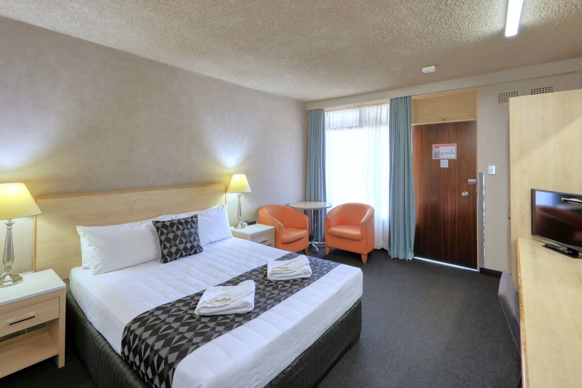 Een hotelkamer met een bed, twee stoelen, een televisie en een bureau met een lamp.