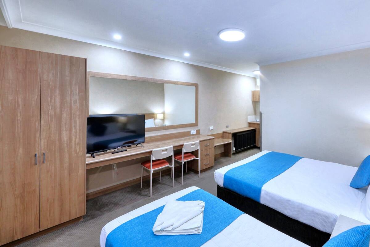 Een hotelkamer met twee bedden, een bureau met een televisie, een stoel en een kledingkast.