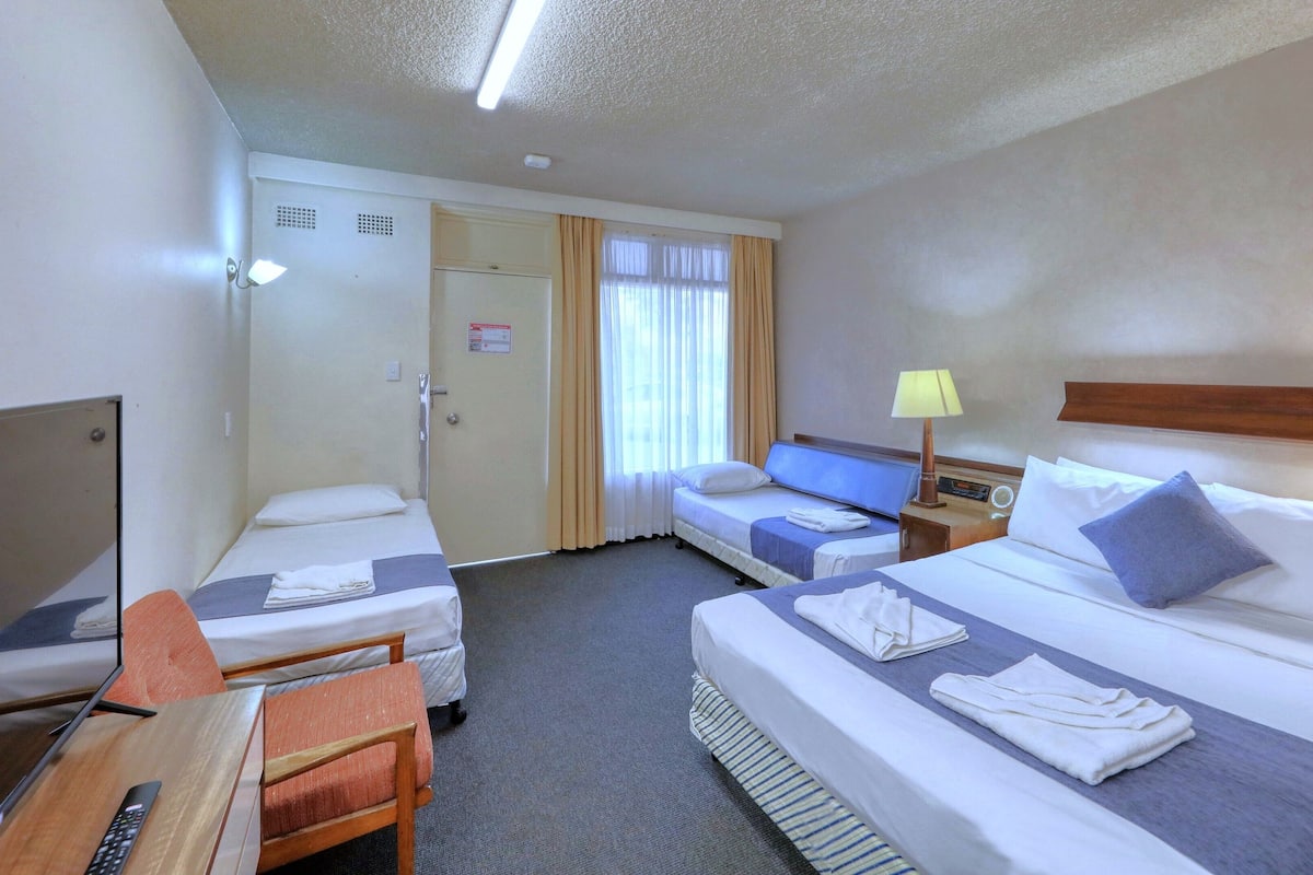 Een hotelkamer met twee bedden, een bureau, een stoel, een televisie en een raam met gordijnen.