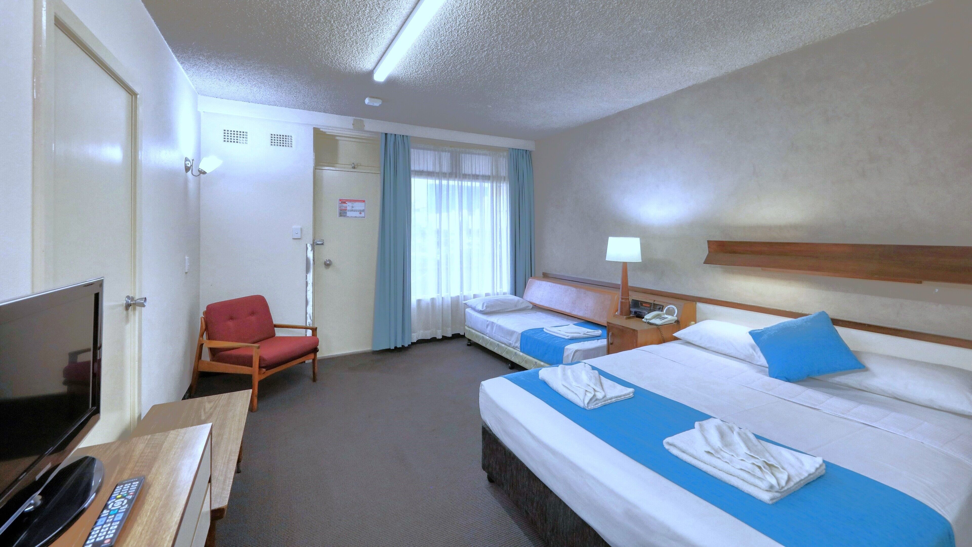 A hotel room with two beds, a TV, a chair, and a desk with a remote control.
