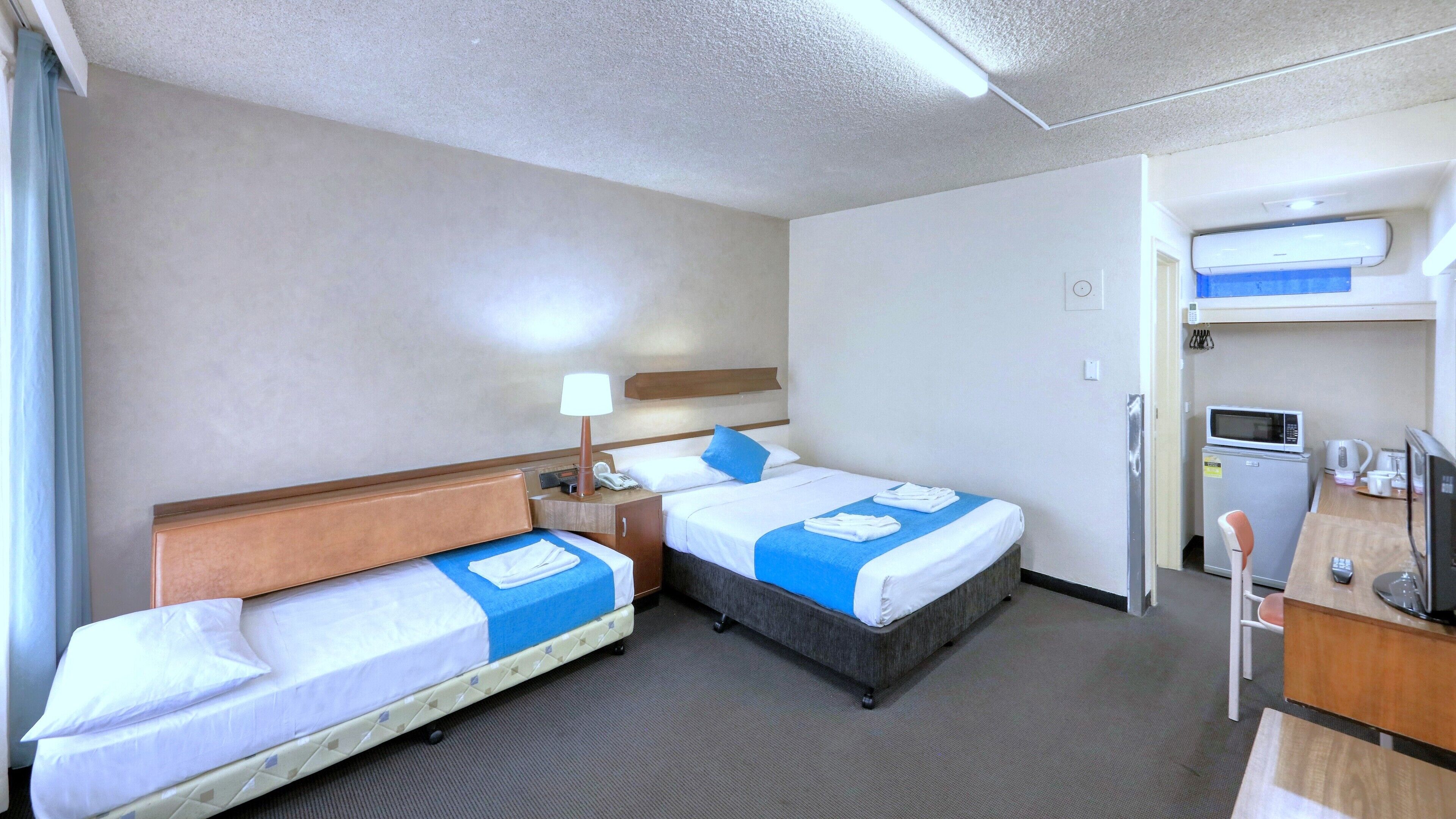 Quarto de hotel com duas camas, uma mesa de trabalho com micro-ondas, cafeteira e pequena geladeira.