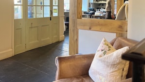 A hotel lobby with a leather sofa, wooden beams, a glass door with a sunburst design, and a person in the background. - Noel Arms Hotel (Chipping Campden)