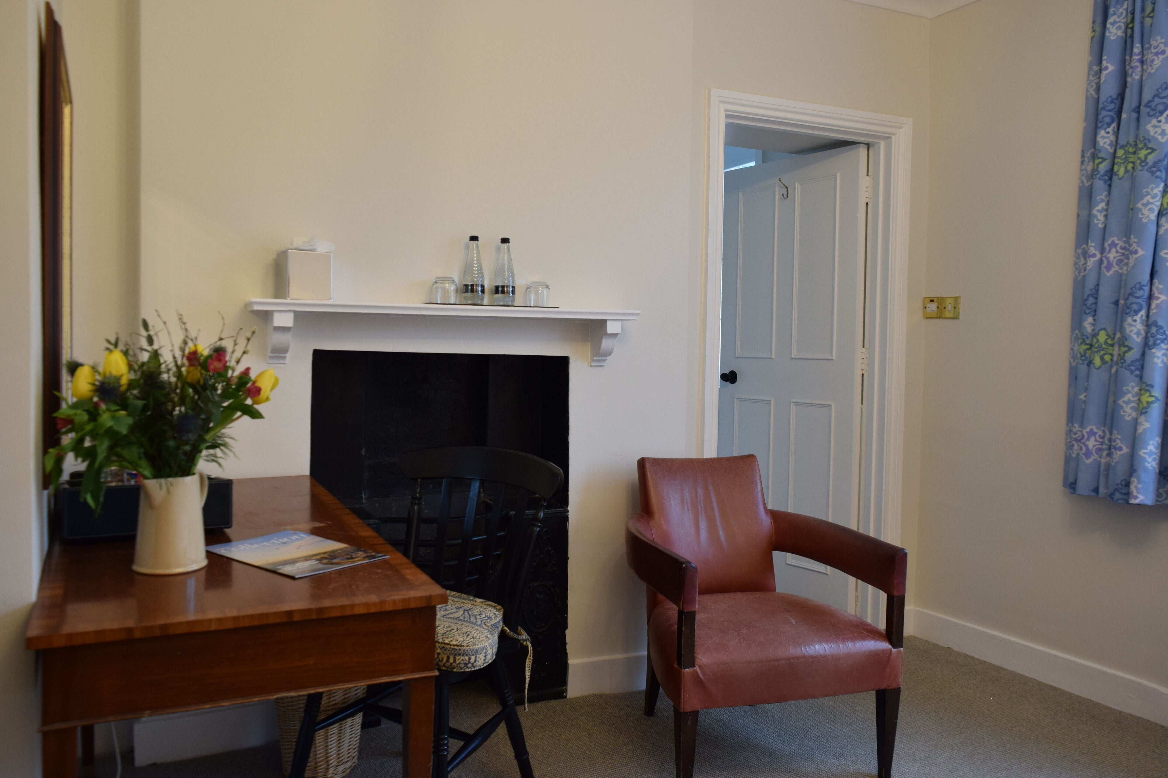 A room with a fireplace, a wooden desk, a leather chair, and a door leading to another room.