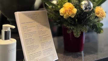 A reception area with a menu for body treatments, a lamp, a flower arrangement, and a bottle of lotion.