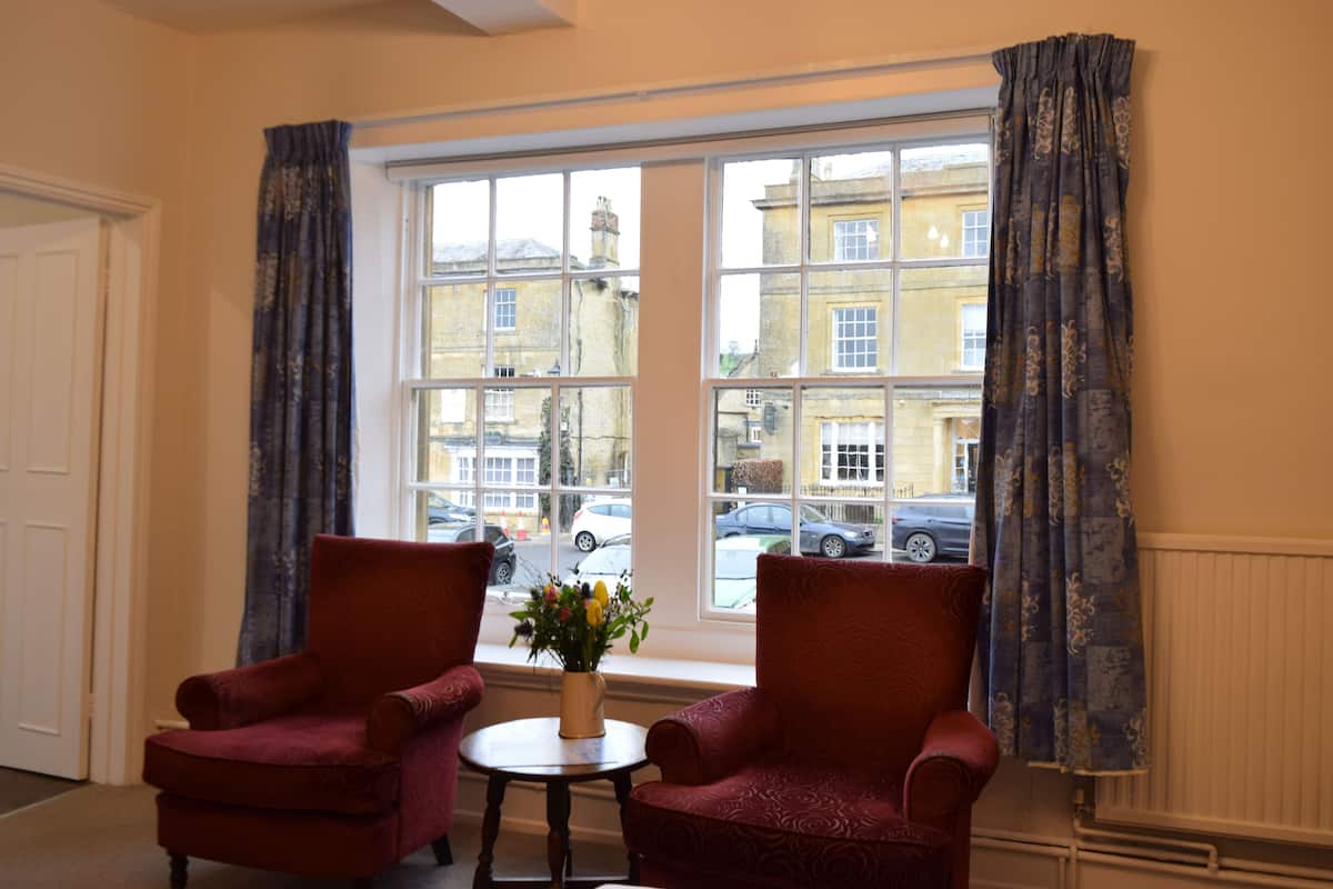 A room with two armchairs, a small table with a vase of flowers, and a large window with curtains.