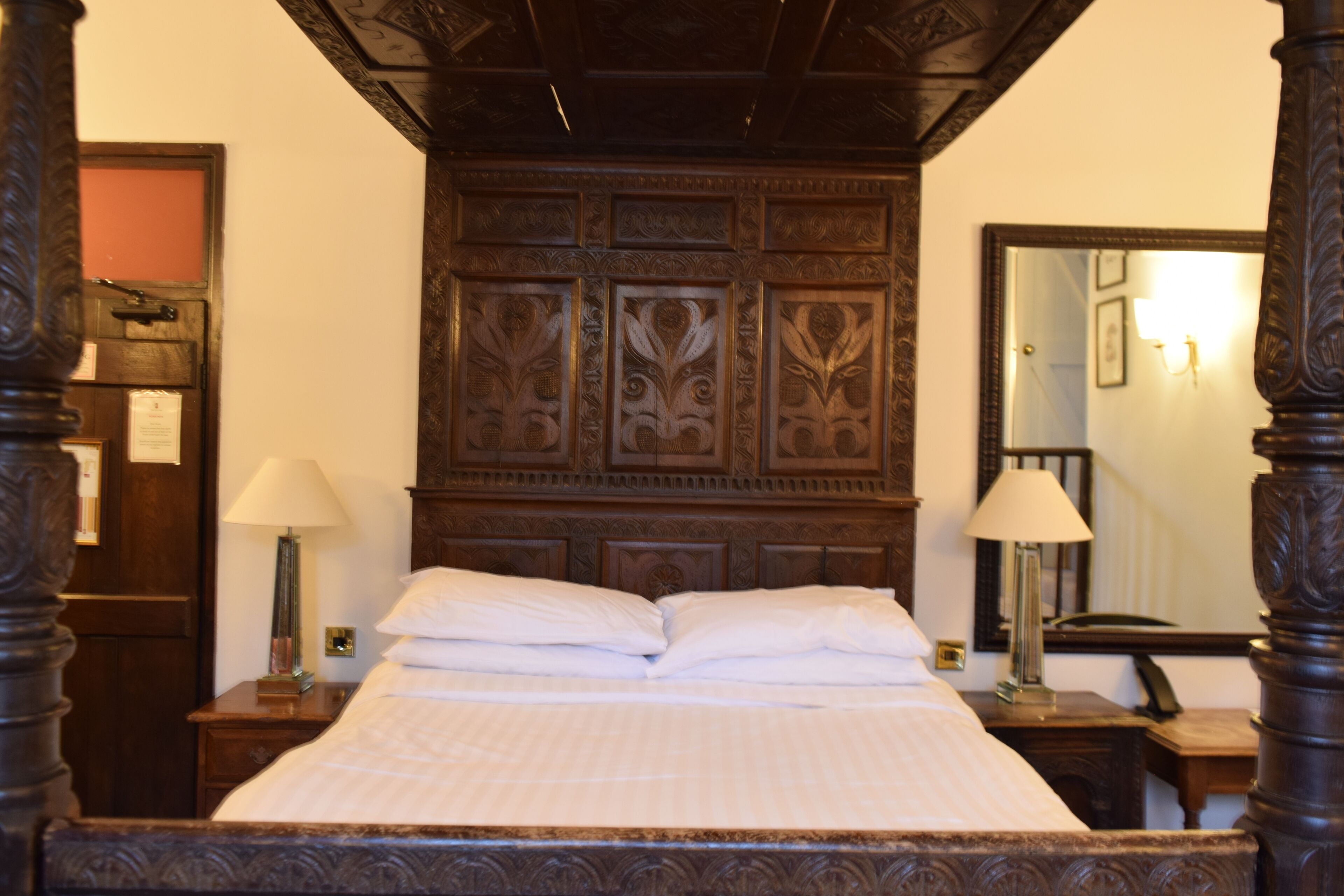 A traditional wooden four-poster bed with a decorative headboard, two bedside tables with lamps, and a mirror on the wall.