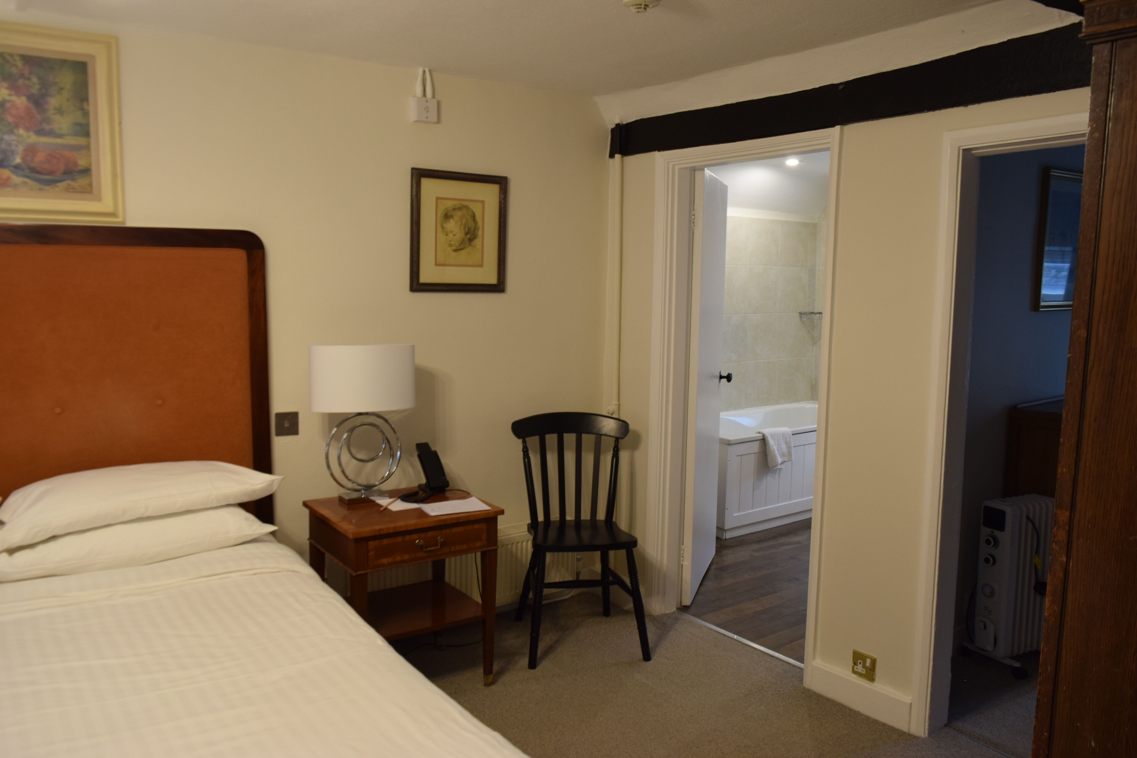Hotelkamer met een bed, een bureau met lamp, een stoel en een zichtbare badkamer door een geopende deur.