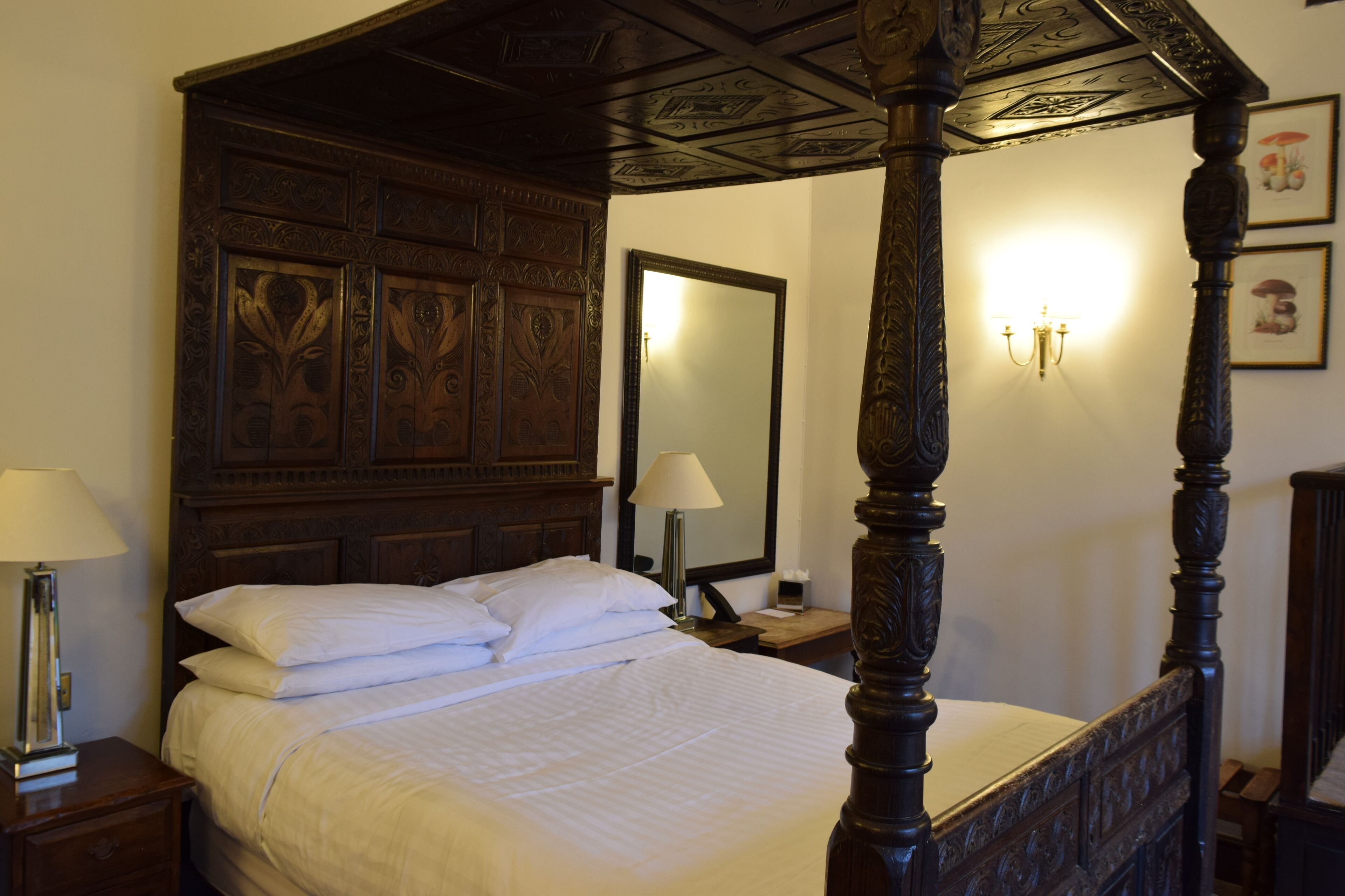 A four-poster bed with a wooden headboard, a bedside table with a lamp, and a nightstand with a mirror.