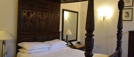 A four-poster bed with a wooden headboard, a bedside table with a lamp, and a nightstand with a mirror.