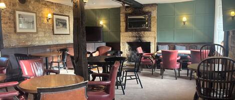 A cozy restaurant interior with wooden tables and chairs, stone walls, and a fireplace.