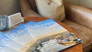 A leather armchair with a pillow, a magazine on a table, and a bookshelf in the background. - Noel Arms Hotel (Chipping Campden)