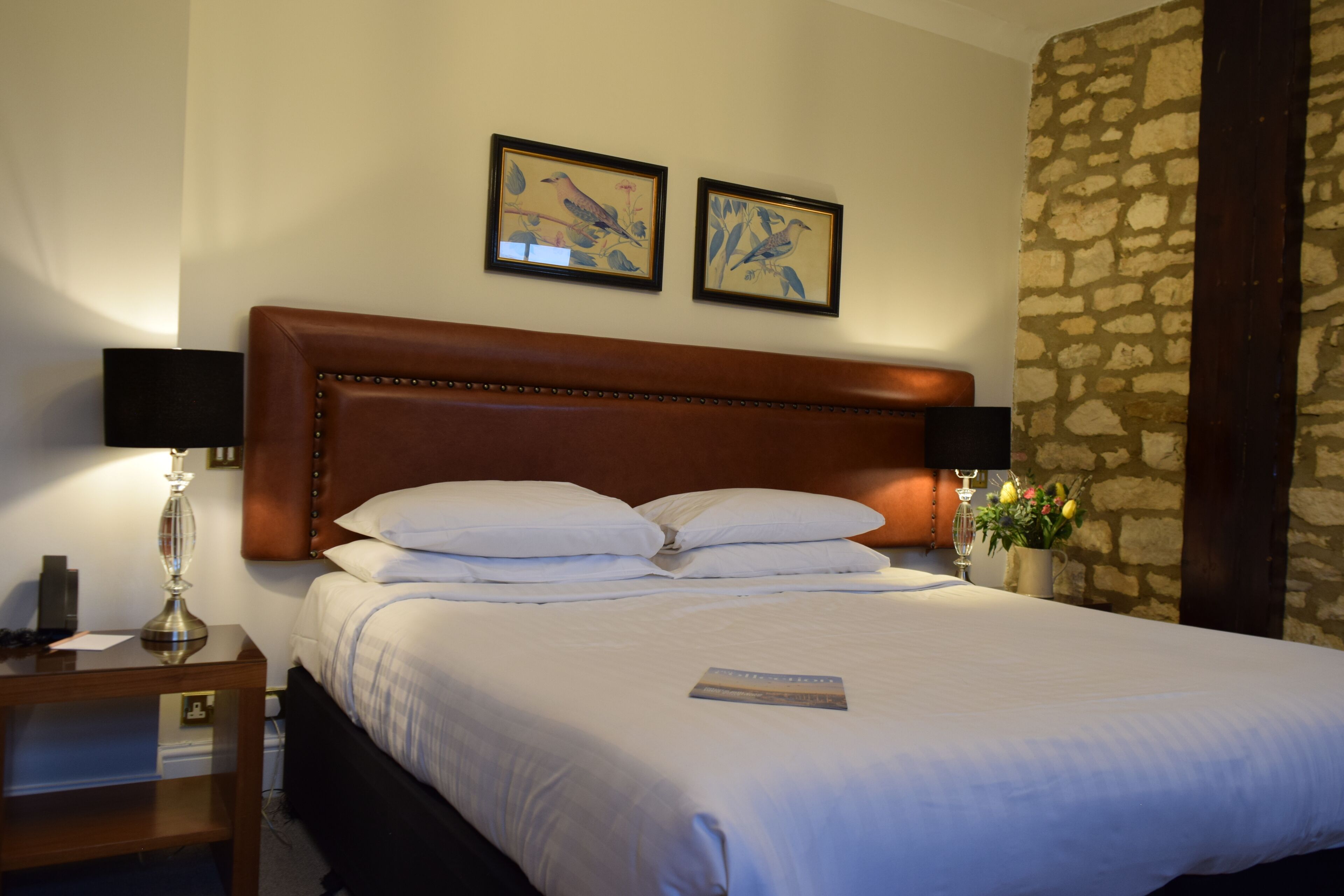 A neatly made bed with white linens, a wooden headboard, and two framed pictures on the wall.