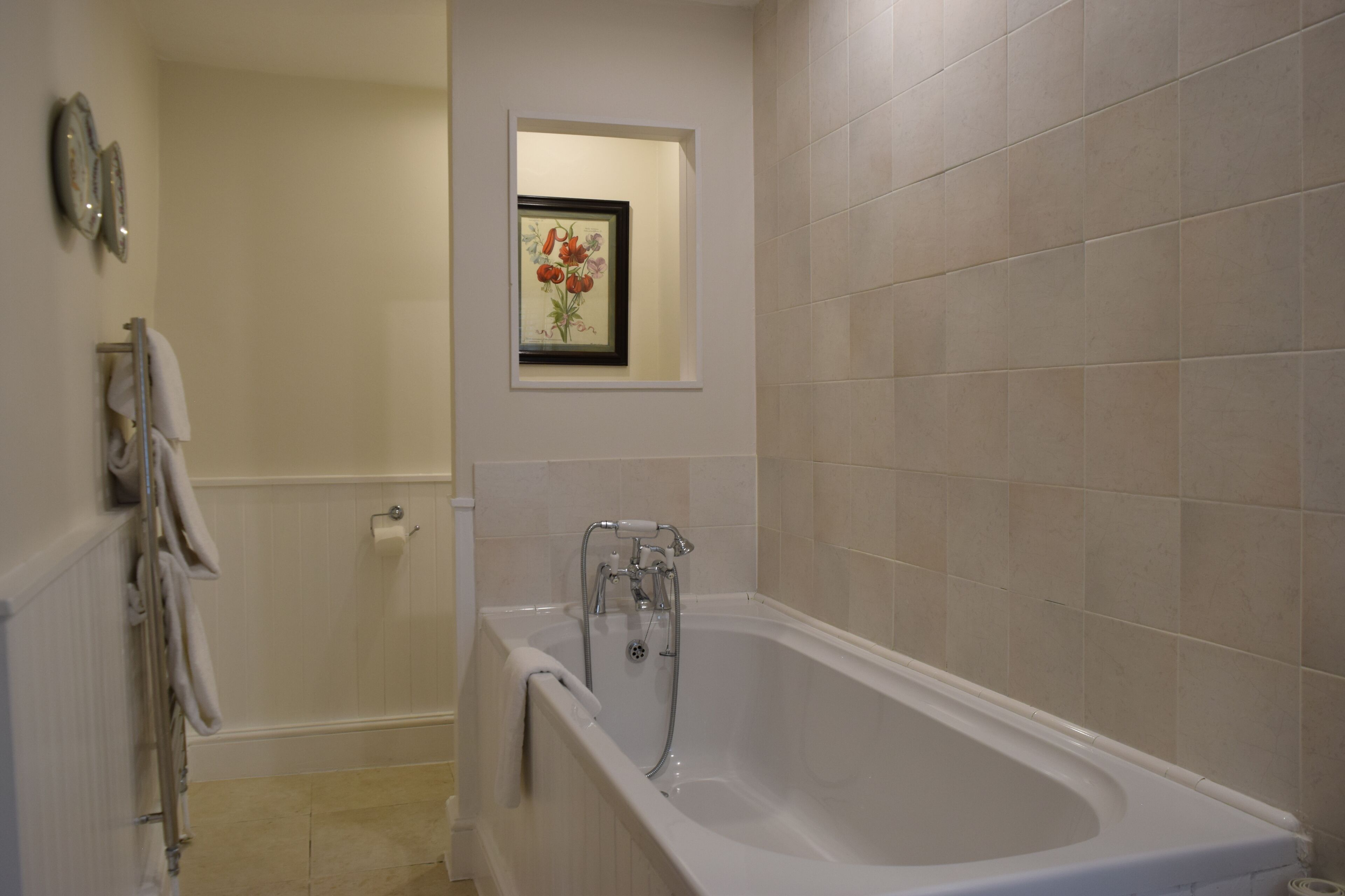 Un baño con bañera, un perchero para toallas y un cuadro en la pared.