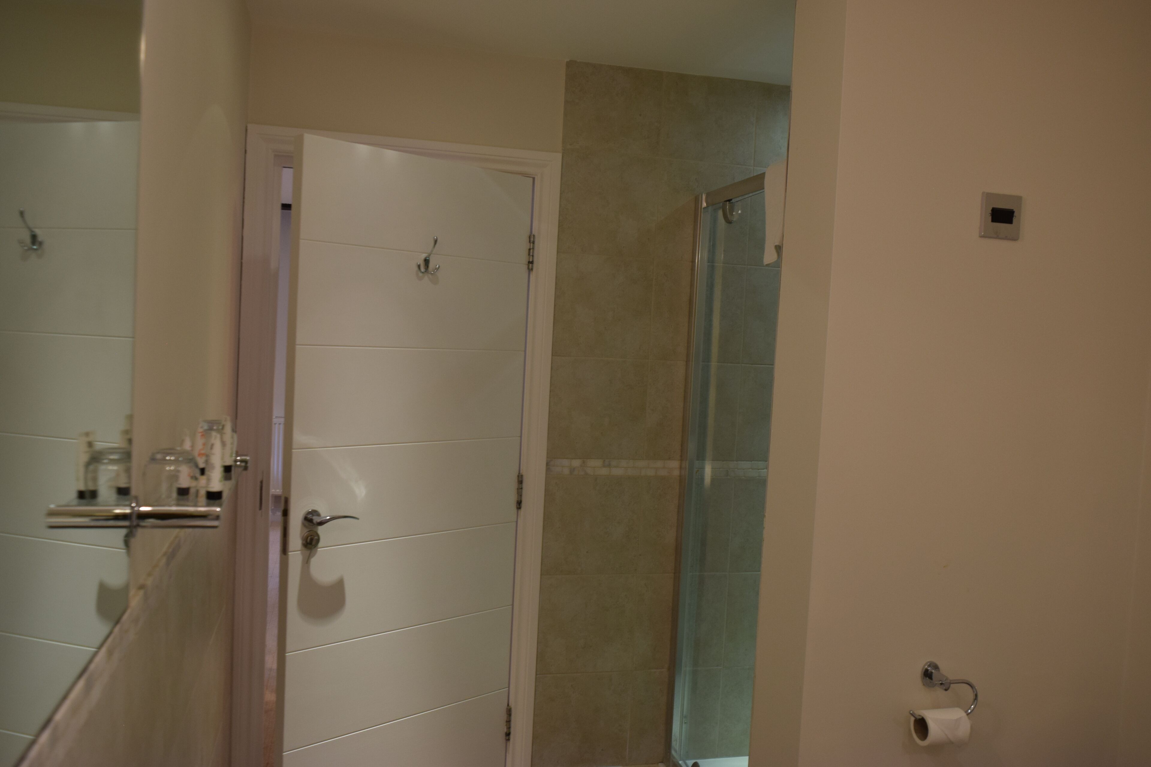 A bathroom with a white door, a glass shower enclosure, and a toilet paper holder on the wall.