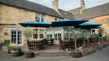 Relax in the serene outdoor seating area with comfortable tables and chairs under shaded umbrellas, surrounded by lush greenery.
