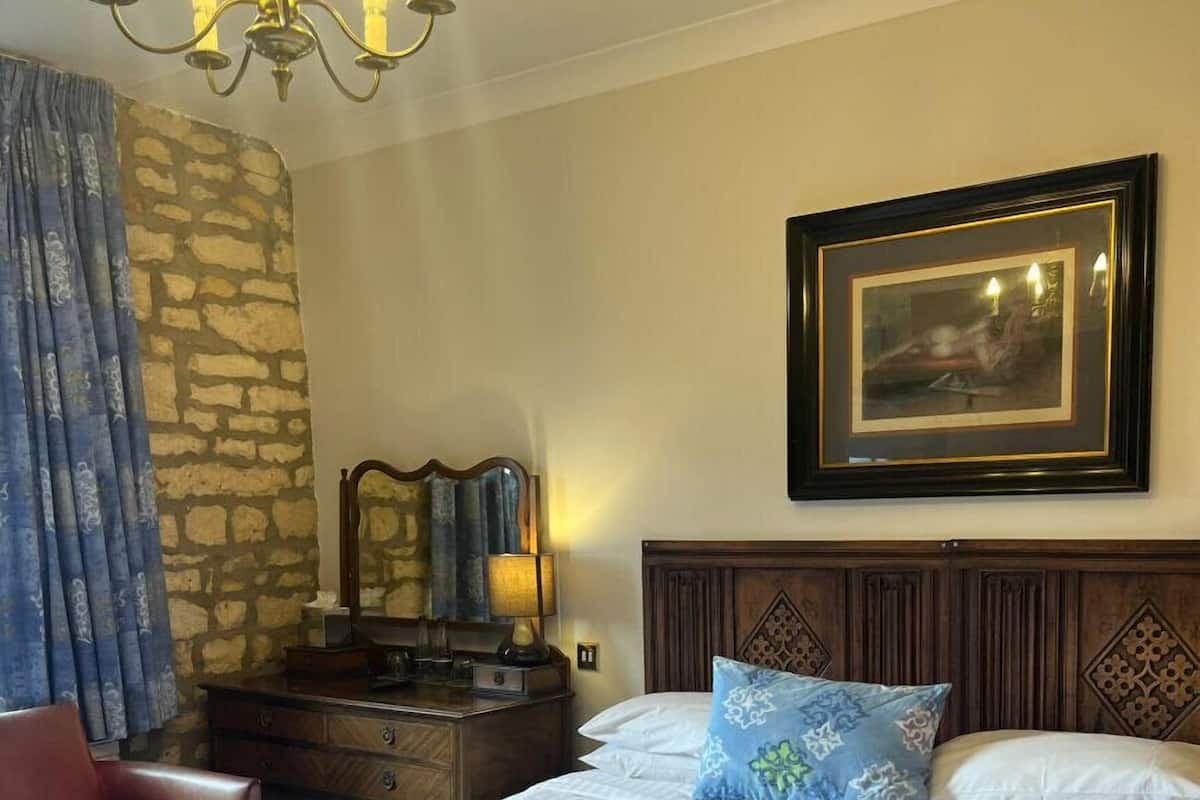 A hotel room with a large bed, a wooden headboard, a dresser, a mirror, a chandelier, and a framed picture on the wall.